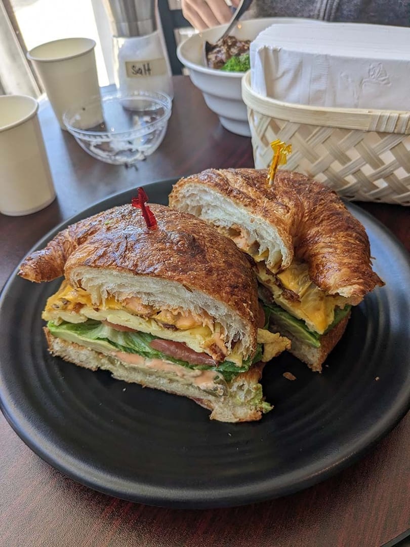Two halves of a croissant sandwich with egg, lettuce, tomato, and sauce on a black plate.