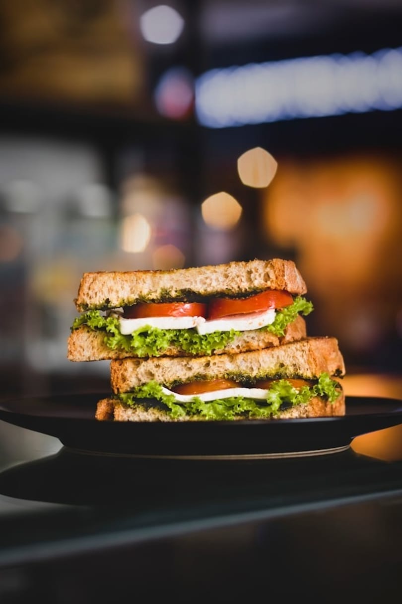 Two halves of a pesto, mozzarella, tomato, and lettuce sandwich on a dark plate.